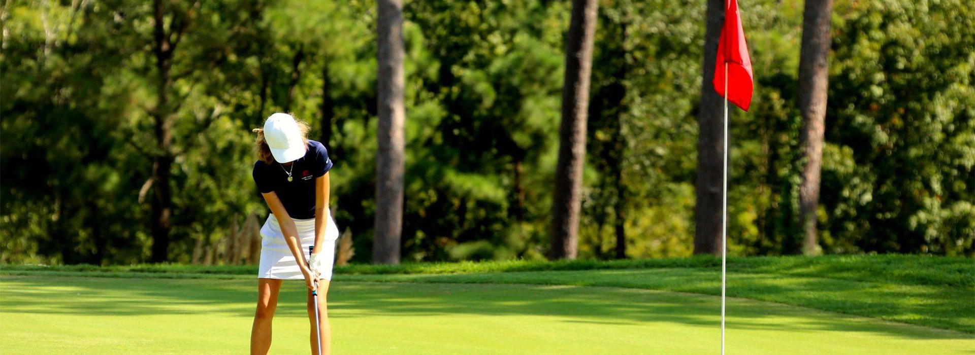 Golfer on golf course green near red flag over hole